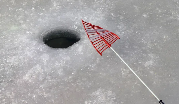 Ice fishing in winter. An ice hole and fishing rod in a frozen lake.