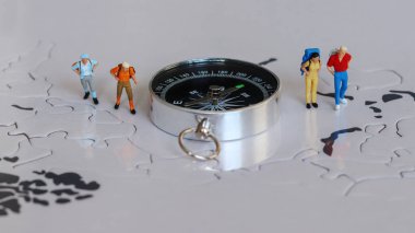 Dört minyatür turist bir pusulanın yanında duruyor..