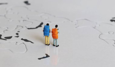 Bir dünya haritasında sırt çantasıyla duran iki minyatür turist.