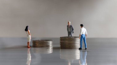 Minyatür bir adam ve minyatür bir kadın farklı yükseklikteki bozuk paraların önünde duruyorlar..