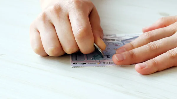 A hand scratching an instant lottery with coins