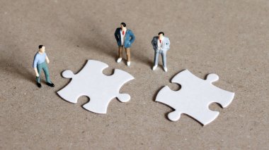 Üç minyatür adam bulmacanın iki parçasına bakıyor..