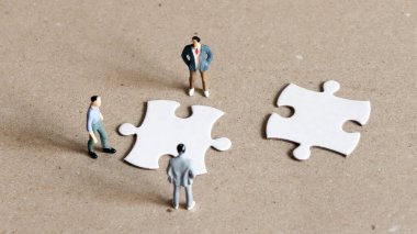 Üç minyatür adam bulmacanın iki parçasına bakıyor..