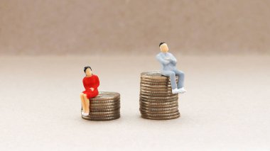 Cinsiyet ayrımcılığı kavramı. Minyatür bir kadın ve bozuk para yığınının üzerinde oturan bir adam..