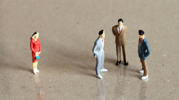 Миниатюрная женщина, стоящая отдельно от группы из трех миниатюрных мужчин
.