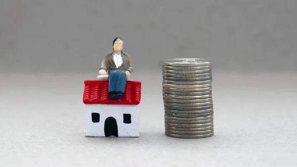 一个矮小的男人坐在一堆硬币旁边的一座小房子上 — 图库照片
