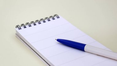 Yumuşak sarı arkaplanda tel kaplı defter ve tükenmez kalem.