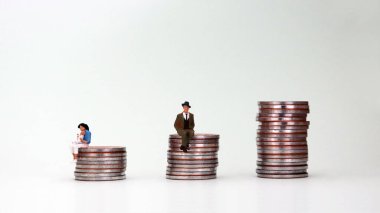 Bozuk para yığınının üzerinde oturan minyatür bir adam ve bozuk para yığınının üzerinde oturan minyatür bir kadın. Cinsiyet maaş farkı kavramı.