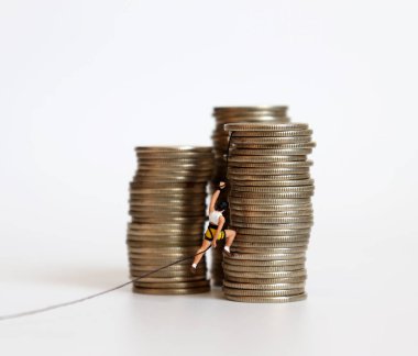 Minyatür bir kadın bozuk para yığınının üzerinde iple tırmanmaya çalışıyor. Zengin ve fakir ve rekabet arasındaki uçurum kavramı.