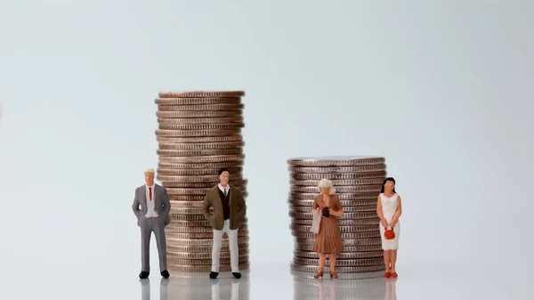 The concept of gender pay discrimination. Miniature men and women standing next to a pile of coins of different heights.
