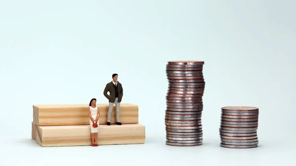 The concept of gender pay gap. A miniature man and a miniature woman standing next to two piles of coins.