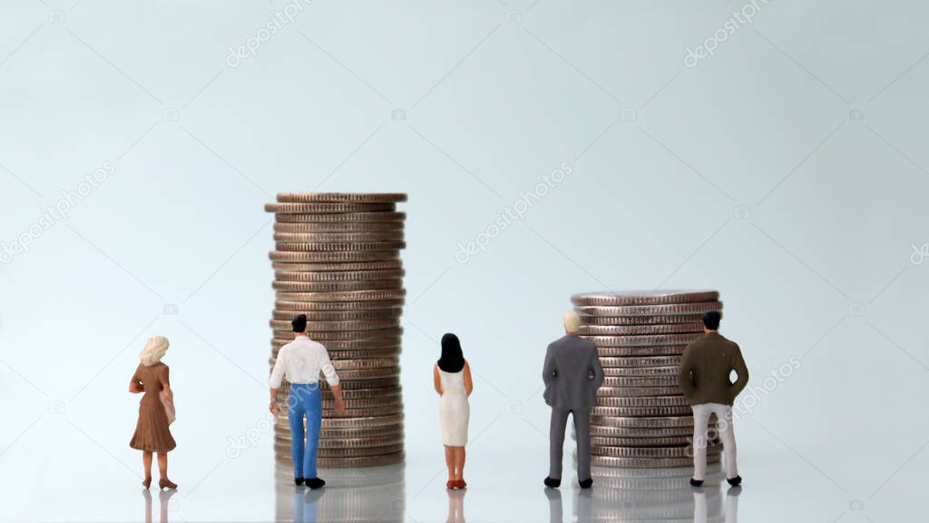 Five miniature people standing in front of a pile of coins.