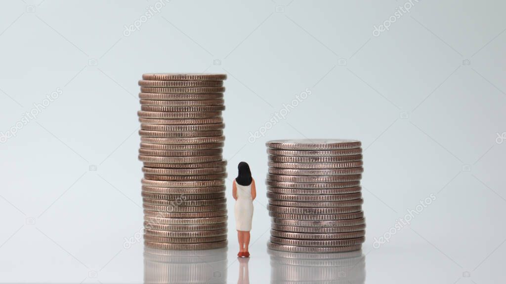 The back of a miniature woman watching two pile of coins.