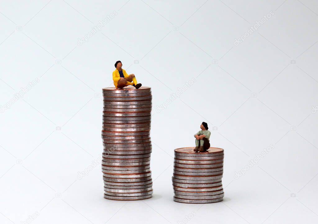 The concept of gender pay gap. A miniature man and a miniature woman sitting on piles of coins.