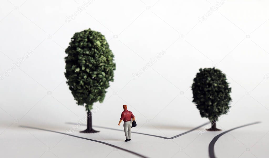 A miniature man walking towards a large tree.