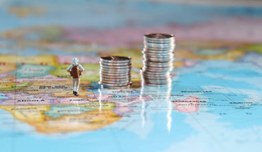 Minyatür insanlar iki bozuk para yığınıyla haritanın üzerinde duruyorlar. Seyahat ve maliyet kavramı.