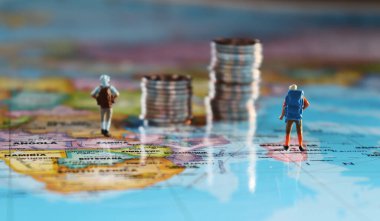 Minyatür insanlar iki bozuk para yığınıyla haritanın üzerinde duruyorlar. Seyahat ve maliyet kavramı.