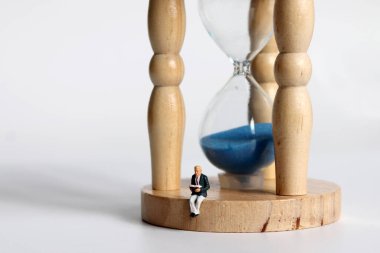 Kum saatinde oturmuş kitap okuyan minyatür bir adam..