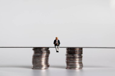 İki bozuk para yığınının arasında oturmuş kitap okuyan minyatür bir adam..