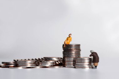 Bozuk para yığını tutan minyatür bir kadın ve bozuk para yığınının üzerinde oturan minyatür bir kadın..