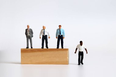 Ağaçların üzerinde duran minyatür insanlar ve ağaç bloklarının altında duran minyatür adam. İstihdam ve tanıtımda ırk ayrımcılığı kavramı.