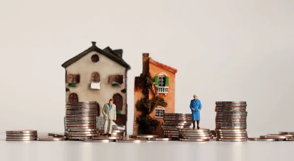 Miniature old people with a pile of coins in front of the miniature house.