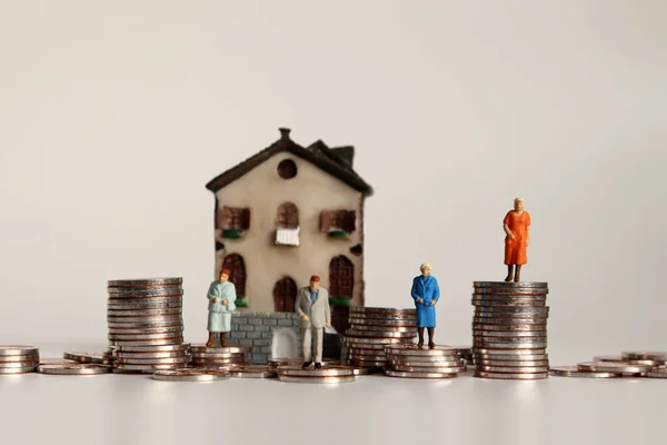 Miniature old people with a pile of coins in front of the miniature house.