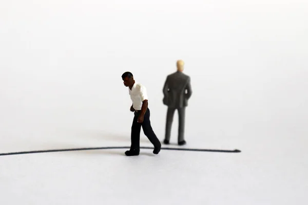 The concept of racial conflict. A miniature black man and a miniature white man standing back from each other with boundaries between them.