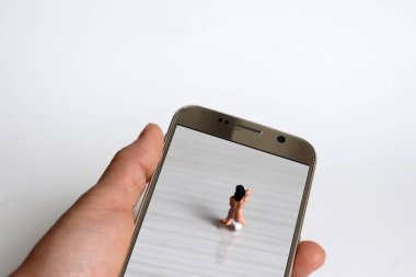 Elbiselerini değiştiren minyatür bir kadının arkası. Minyatür insanlar ve Akıllı Telefon. 