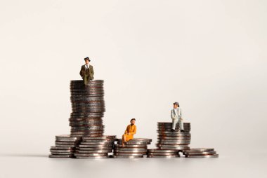 Madeni paraların üzerinde oturan minyatür insanlar. Gelir dağılımı açığı kavramı.