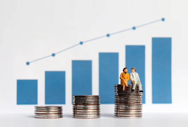 The concept of aging society and rising costs. Blue bar graph with flow linear graph. The stack of coins and miniature older people.