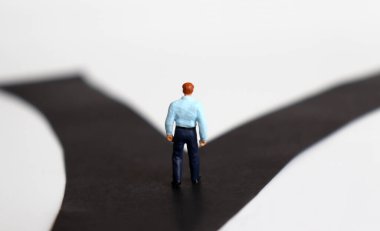 İki çatal yolun önünde duran minyatür bir adamın arkası..