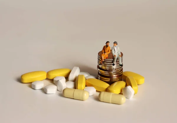 An old miniature couple and pills sitting on a pile of coins.