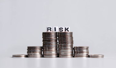 Bozuk para yığınının üzerinde 'RISK' metni beyaz küp.