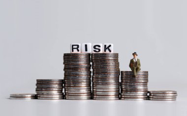 'RISK' mesajı beyaz küp ve bozuk para yığınının üzerinde oturan minyatür bir adam.