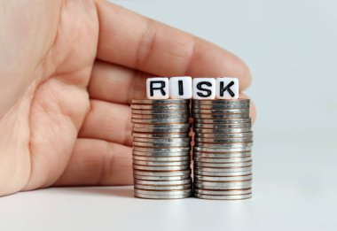 'RISK' metnini saran bir el, iki bozuk para yığınına beyaz küp..