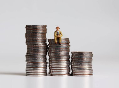 Bozuk para yığınının üzerinde oturan minyatür bir adam..