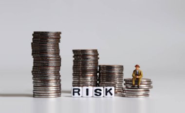'RISK' mesajı beyaz küp ve bozuk para yığınının üzerinde oturan minyatür bir adam.