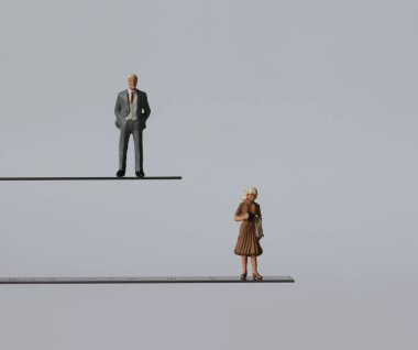 Farklı yüksekliklerde duran minyatür bir adamla minyatür bir kadın. Cinsiyete göre istihdamda ayrımcılık kavramı.