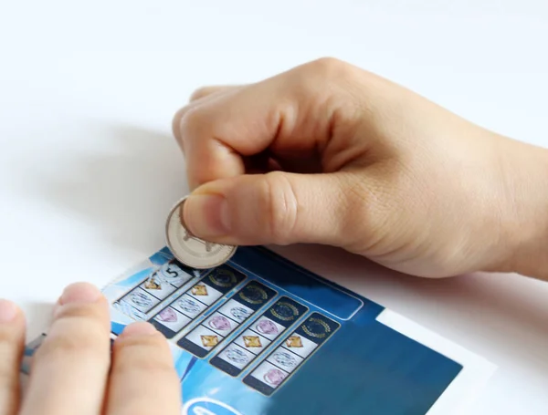 A woman\'s hand scratching an instant lottery ticket with a coin.