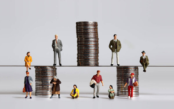 Miniature people and piles of coins. The concept of wealth gap and social stratification.