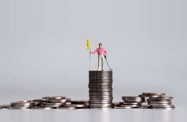 Elinde golf sopası ve bozuk paraların üzerinde bayrak olan minyatür bir golfçü..