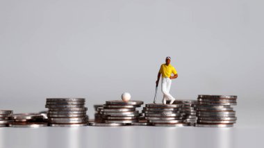 Bozuk para yığınının üzerinde duran minyatür golfçü.