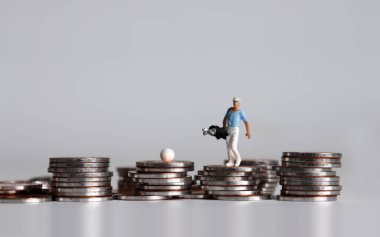 Elinde golf çantasıyla bozuk paraların üzerinde yürüyen minyatür bir adam..