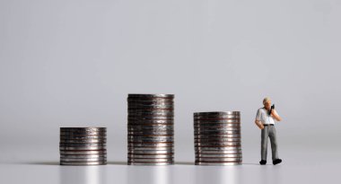 Minyatür bir adam telefonda üç yığın bozuk parayla konuşuyor..