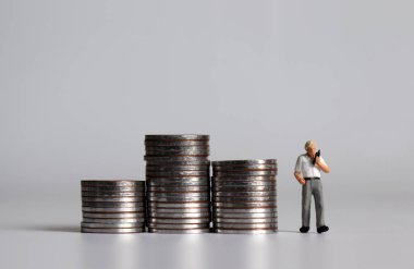 Minyatür bir adam telefonda üç yığın bozuk parayla konuşuyor..