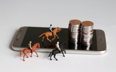 Minyatür bir adam ata biniyor. Akıllı telefon ve bozuk para yığınları.