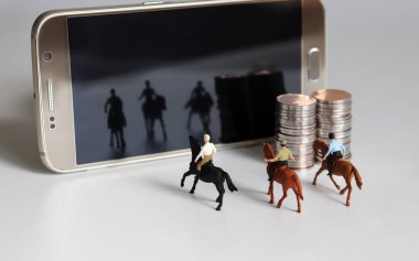 Minyatür bir adam ata biniyor. Akıllı telefon ve bozuk para yığını.