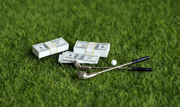 A bundle of money and golf equipment on the green grass.