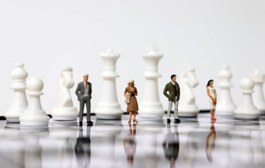 Satranç tahtasında satranç taşlarıyla duran minyatür insanlar..